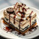 A slice of layered ice cream sandwich cake with whipped topping, chocolate syrup and cookie crumbs.